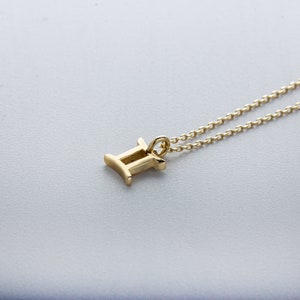 May include: A gold chain necklace with a Gemini zodiac sign pendant. The pendant is a simple, stylized design of the Gemini symbol.