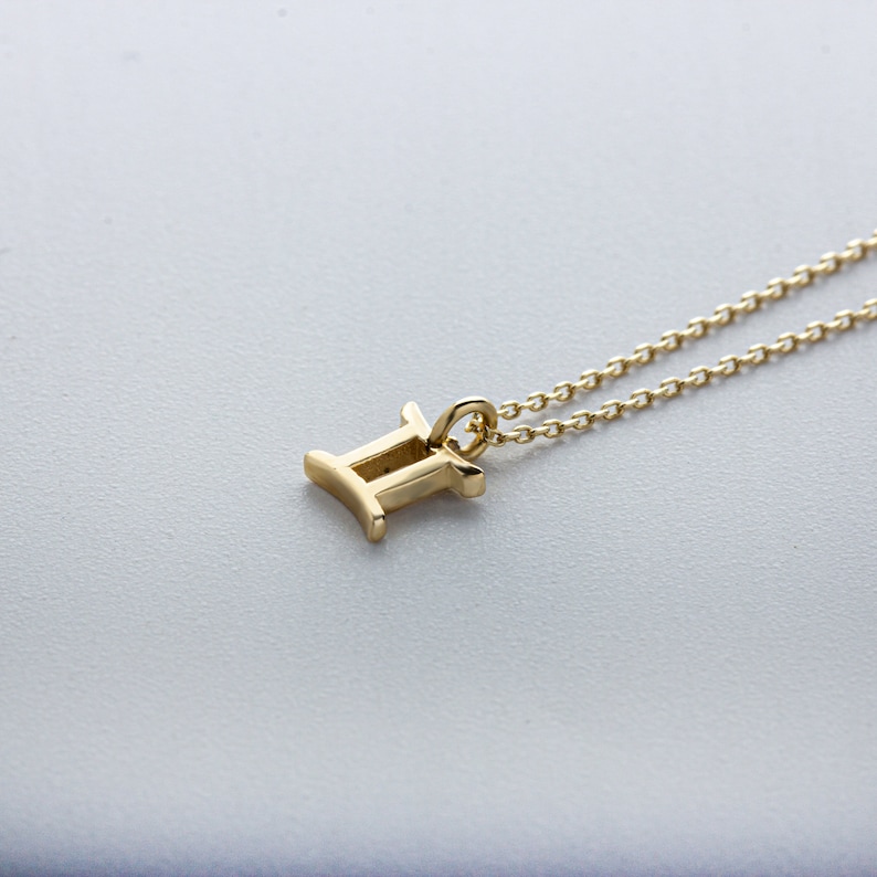 May include: A gold chain necklace with a Gemini zodiac sign pendant. The pendant is a simple, stylized design of the Gemini symbol.