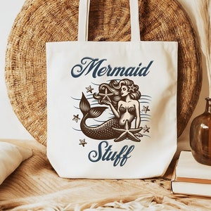 May include: White canvas tote bag with a mermaid illustration and the text "Mermaid Stuff".