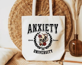 May include: White canvas tote bag with black text that reads "Anxiety University" with a skull and snake graphic and the words "Honors Program" below.