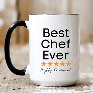 May include: White ceramic mug with a black handle and rim. The mug features the text "Best Chef Ever" in black, with five orange stars and the words "Highly Recommend" below.