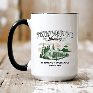 May include: White ceramic mug with a black handle. The mug has a graphic of a cabin in the woods with the text "Yellowstone Roastery, Wyoming Montana, Quality Made".