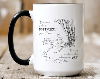 May include: White ceramic mug with a black handle. The mug features a black and white illustration of Winnie the Pooh and Piglet walking in the woods. The quote "It makes such a DIFFERENCE, said Pooh, To have someone who believes in YOU." is printed on the mug.