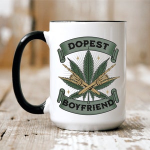 May include: White ceramic mug with a black handle and rim. The mug features a green cannabis leaf design with crossed skeleton hands and the words "Dopest Boyfriend" in a banner.