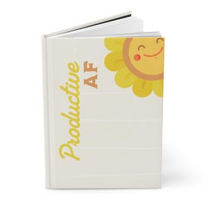 Peut inclure: Un journal blanc avec un motif de tournesol jaune et le texte "Productive AF" sur la couverture.