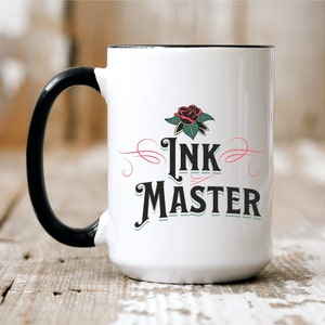 May include: White ceramic mug with a black handle. The mug has a black rim and features a stylized rose tattoo design with the text "Ink Master" in a vintage font.