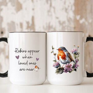 May include: White ceramic mug with a black handle. The mug has a robin bird with flowers on one side and the text "Robins appear when loved ones are near." with two purple hearts on the other side.
