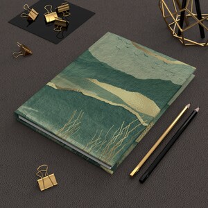 May include: A green and gold journal with a landscape design. The journal has a textured cover and a white spine.