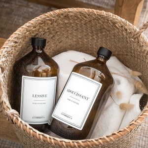 May include: Two amber glass bottles with white labels in a woven basket. The labels read "Lessive Pure & Naturel La Fabrique" and "Adoucissant Pure & Naturel La Fabrique".