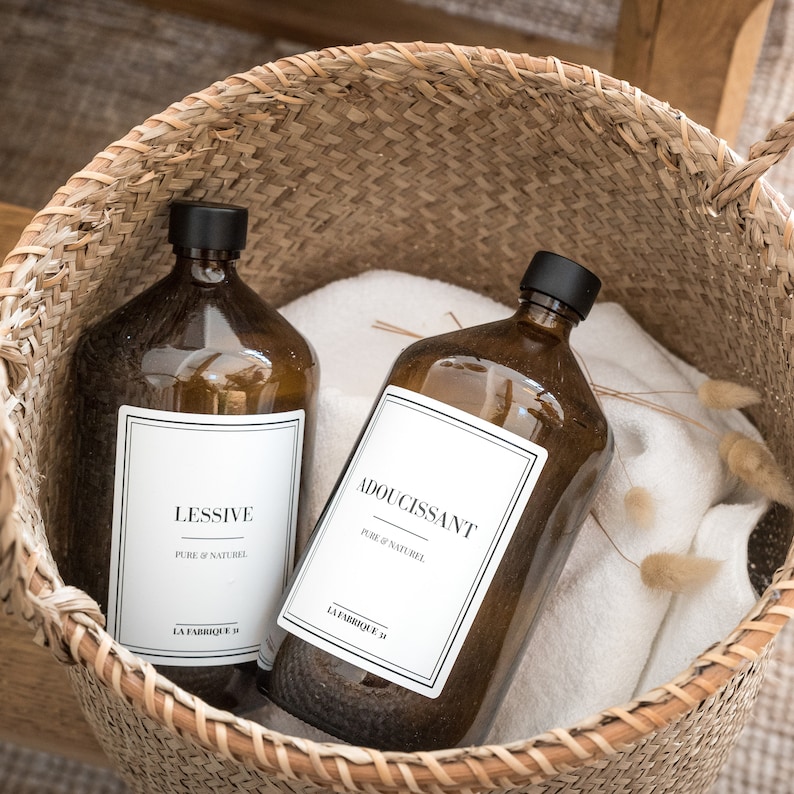 May include: Two amber glass bottles with white labels in a woven basket. The labels read "Lessive Pure & Naturel La Fabrique" and "Adoucissant Pure & Naturel La Fabrique".