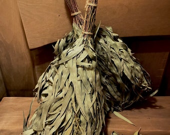 May include: Two bundles of dried eucalyptus leaves tied together with twine, resting on a wooden surface. The leaves are a light green colour and are arranged in a loose, natural way.