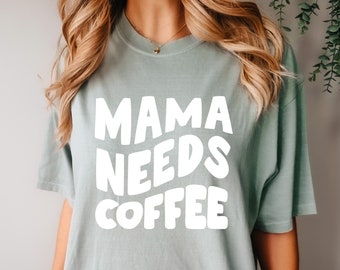 May include: A light blue t-shirt with the text "MAMA NEEDS COFFEE" in white, stylised lettering.