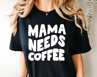 May include: Black t-shirt with white text that reads "Mama Needs Coffee" in a playful, rounded font.