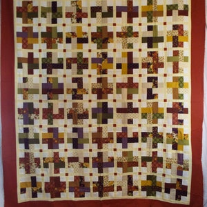 May include: A quilt with a patchwork design featuring a variety of floral and geometric patterns in shades of brown, green, yellow, and purple. The quilt is framed with a red border.