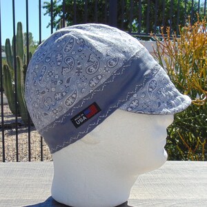 May include: A light blue welding cap with a paisley pattern and a dark blue band. The cap has a small brim and a tag that reads "MADE IN USA". The cap is displayed on a white mannequin head.