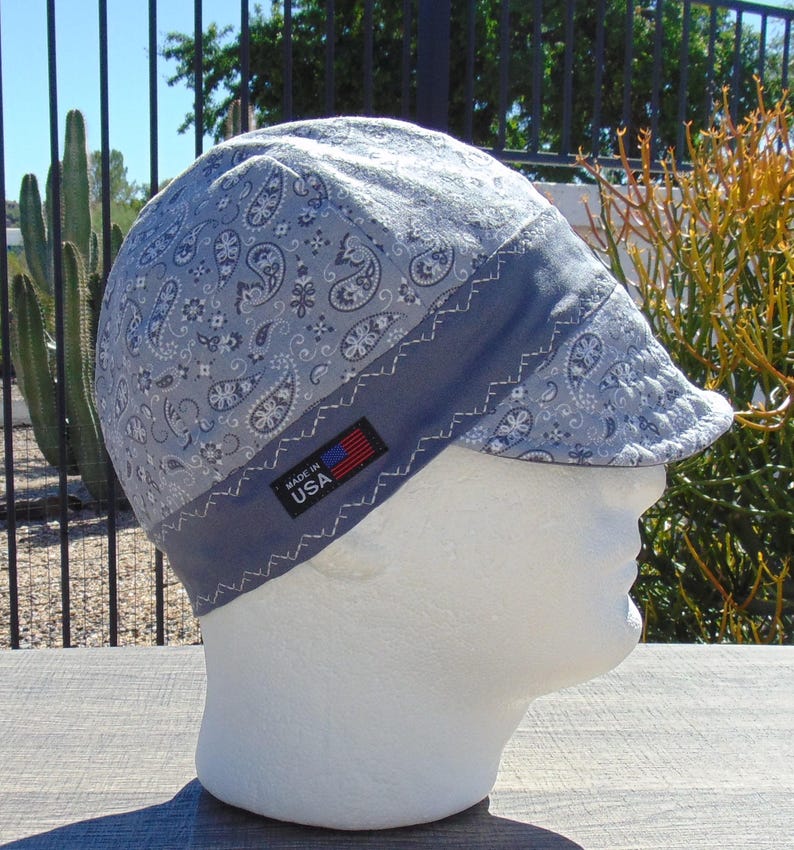 May include: A light blue welding cap with a paisley pattern and a dark blue band. The cap has a small brim and a tag that reads "MADE IN USA". The cap is displayed on a white mannequin head.