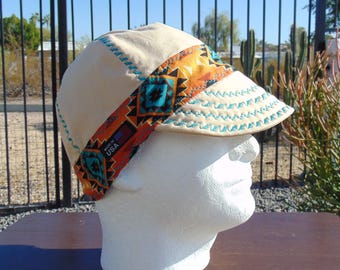 May include: A tan canvas work cap with a turquoise, orange, and black patterned band. The band has the text "Made in USA" on it. The cap has a turquoise stitching detail around the brim.