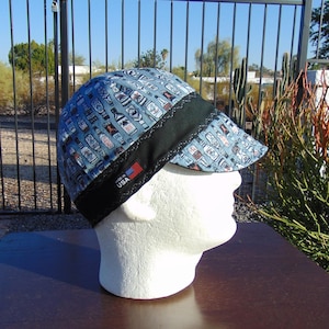 May include: A blue and black patterned welding cap with a black brim and a black strap. The cap has a white label with the text "Made in USA" and a small American flag.