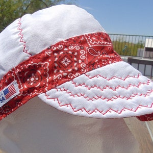 May include: White cotton welding cap with a red bandana trim and a zig-zag stitch detail. The bandana has a paisley pattern and a small American flag patch. "Made in USA" is printed on the patch.