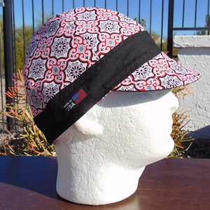 May include: A patterned cap with a black band and a small tag with the American flag and the text "MADE IN USA". The cap features a repeating floral design in red, black, and white.