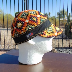 May include: A black and orange patterned welding cap with a black brim and a "Made in USA" label. The cap is on a white mannequin head.