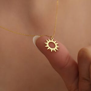 以下が含まれることがあります： 太陽のペンダントが付いたゴールドネックレス。ペンダントは、縁から放射状に伸びる光線を持つシンプルなオープンサークルです。