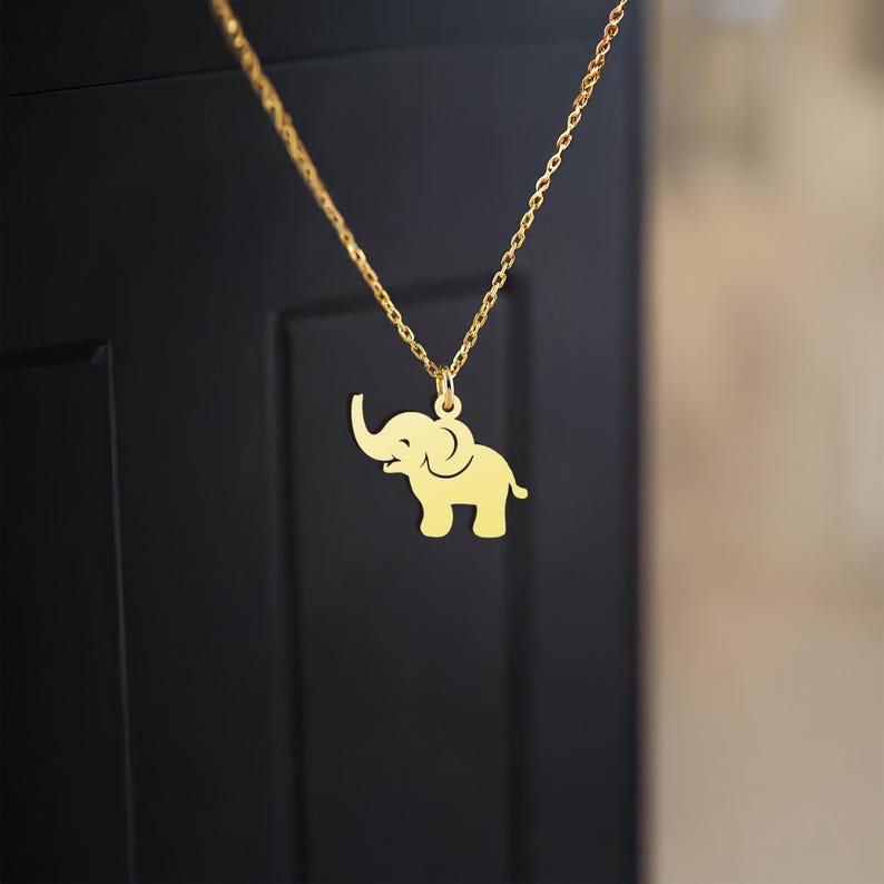 K&ouml;nnte beinhalten: Eine goldene Kettenkette mit einem Elefantenanh&auml;nger. Der Elefant ist nach rechts gerichtet und hat seinen R&uuml;ssel erhoben.