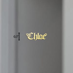 May include: Gold-colored metal charm with the name "Chloe" in a gothic font. The charm is 0.3 inches tall.