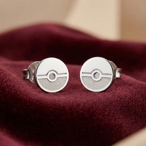 Peut inclure: Une paire de boucles d'oreilles &agrave; clous circulaires en argent pr&eacute;sentant un design divis&eacute; avec une moiti&eacute; sup&eacute;rieure polie lisse et une moiti&eacute; inf&eacute;rieure mate textur&eacute;e, s&eacute;par&eacute;es par une ligne horizontale et un cercle central.