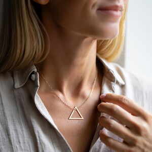 Puede incluir: Un collar de oro con un colgante de tri&aacute;ngulo simple. El collar es delicado y minimalista, lo que lo convierte en una pieza de joyer&iacute;a perfecta para el d&iacute;a a d&iacute;a.