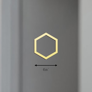 K&ouml;nnte beinhalten: Ein goldfarbenes, sechseckiges Objekt, etwa 1,5 cm breit, wird vor einem grauen Hintergrund dargestellt. Die geometrische Form ist ein sechsseitiges Polygon, wobei eine d&uuml;nne Umrandung seine Form definiert. Das Objekt scheint ein dekoratives Element oder eine Komponente zu sein.