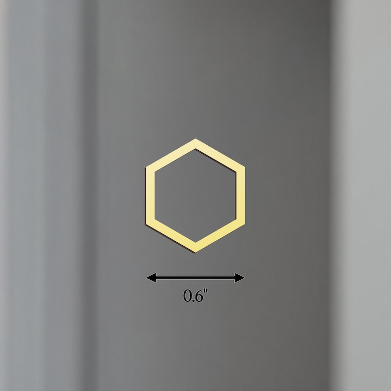 K&ouml;nnte beinhalten: Ein goldfarbenes, sechseckiges Objekt, etwa 1,5 cm breit, wird vor einem grauen Hintergrund dargestellt. Die geometrische Form ist ein sechsseitiges Polygon, wobei eine d&uuml;nne Umrandung seine Form definiert. Das Objekt scheint ein dekoratives Element oder eine Komponente zu sein.