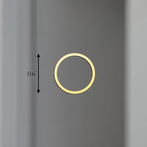 May include: A gold-coloured, circular object, approximately 1.5 cm in diameter, is centered on a grey background. The object is a thin ring, with a consistent width. The overall aesthetic is minimalist and modern.
