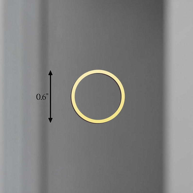 May include: A gold-coloured, circular object, approximately 1.5 cm in diameter, is centered on a grey background. The object is a thin ring, with a consistent width. The overall aesthetic is minimalist and modern.