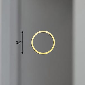 May include: A gold-coloured, circular object, approximately 1.5 cm in diameter, is centered on a grey background. The object is a thin ring, with a consistent width. The overall aesthetic is minimalist and modern.