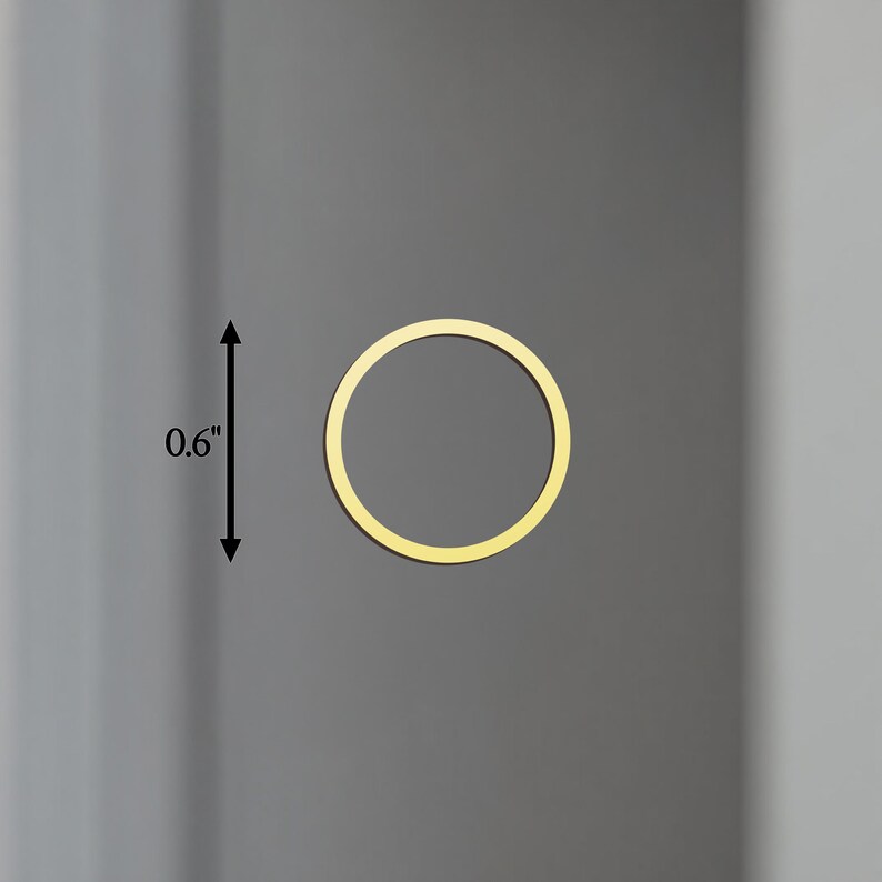 May include: A gold-coloured, circular object, approximately 1.5 cm in diameter, is centered on a grey background. The object is a thin ring, with a consistent width. The overall aesthetic is minimalist and modern.