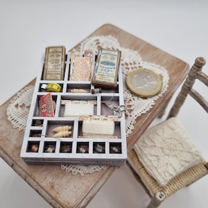Könnte beinhalten: Ein hölzernes Miniatur-Sortierfach gefüllt mit kleinen Nähutensilien wie Garnrollen, Spitze, einem gelben Maßband und einer kleinen Schere. Das Fach enthält gedruckte Etiketten wie Finest Cord und Finest Lace sowie eine Ein-Euro-Münze.
