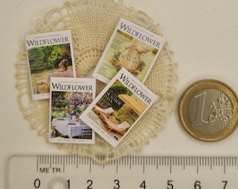 May include: Miniature magazines with the title "WILDFLOWER" are displayed on a lace doily. The magazines feature seasonal covers, including "Autumn" and "Summer Days." A ruler shows measurements in centimeters, and a one Euro coin is next to the magazines.