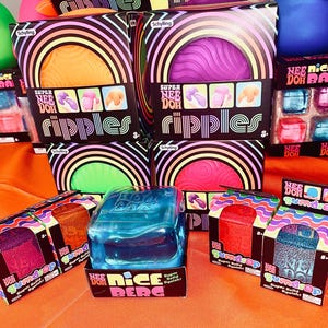 May include: A collection of Schylling Nee Doh sensory toys in various packaging. The boxes feature Super Nee Doh Ripples in orange, purple, green, and pink, alongside Nee Doh Gumdrop and a blue Nee Doh Nice Berg cube, all displayed together.