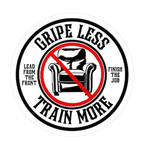 May include: A round sticker with a black and white design. The sticker says "Gripe Less Train More" in a circle around a red circle with a diagonal line through it. Inside the red circle is a black and white illustration of a recliner. The text "Lead from the front" is on the left side of the sticker and "Finish the job" is on the right side.