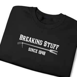May include: Black t-shirt with white text that reads "BREAKING STUFF SINCE 1948" and a graphic of a crowbar.