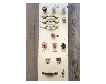May include: A wooden board with 15 different cabinet knobs and pulls. The knobs are made of ceramic, metal, and wood. The pulls are made of metal. The board is labeled with numbers 1 through 15.