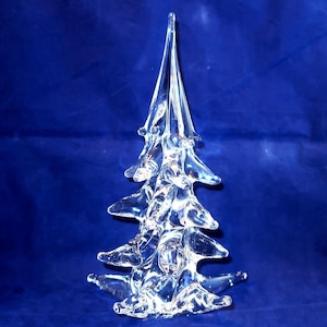 May include: A clear glass sculpture shaped like a stylized evergreen tree. The object features a smooth, transparent surface with multiple tiered, pointed branches extending outward from a central vertical trunk, tapering to a sharp point.