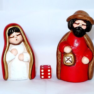 以下が含まれることがあります： マリアとヨセフのフィギュアと赤いサイコロが特徴のセラミック製の降誕シーン。マリアは赤と金のトリムのローブを着ており、ヨセフは赤いローブと茶色のマントを着てランタンを持っています。フィギュアは白い背景にあります。