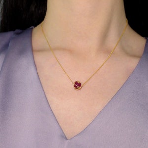 Puede incluir: Un collar de cadena de oro con un colgante de piedra roja. El colgante es una piedra redonda roja engastada en una jaula de oro.