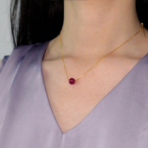 May include: A gold chain necklace with a single, round, dark red gemstone pendant.