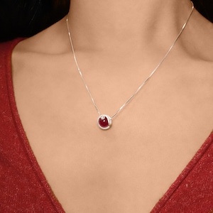 Peut inclure: Un collier en chaîne argent avec un pendentif en pierre rouge. Le pendentif est serti dans un cadre argenté avec un petit accent diamant.