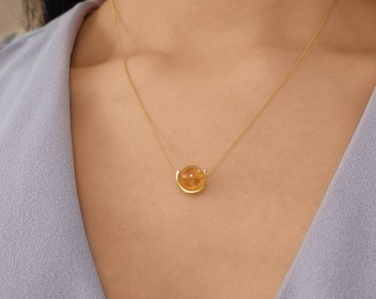 May include: A gold chain necklace with a single, round, yellow gemstone pendant. The pendant is set in a gold, curved, open frame.