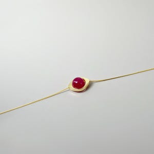 May include: A gold chain necklace with a square pendant featuring a pink gemstone.