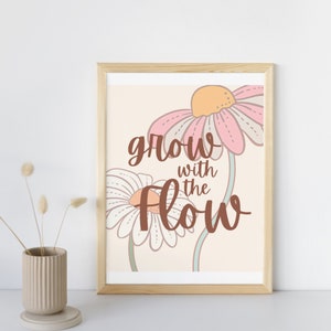 Puede incluir: Una impresión enmarcada con un fondo beige que presenta dos flores estilizadas en rosa y blanco con un texto superpuesto en marrón que dice "grow with the flow".